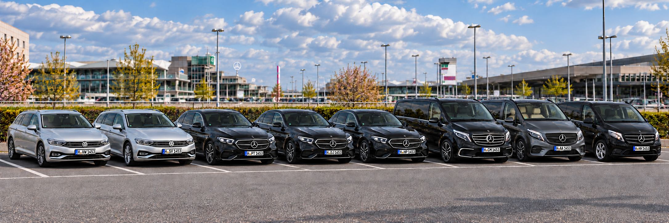 Flottendarstellung: zwei silberne VW Passat Kombi, drei schwarze Mercedes-Benz E-Klasse, eine schwarze V-Klasse, eine graue V-Klasse mit beigem Innenraum und ein schwarzer Vito nebeneinander im Parkbereich